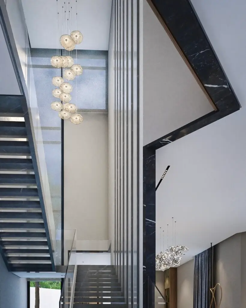 Stair void with a cluster pendant light, black marble frame and slim vertical fins